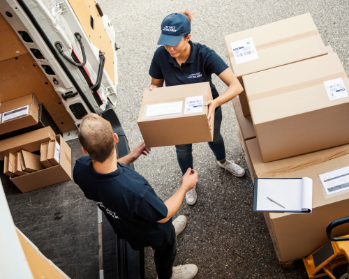 Eine Frau und ein Mann beladen einen Transporter mit Paketen.