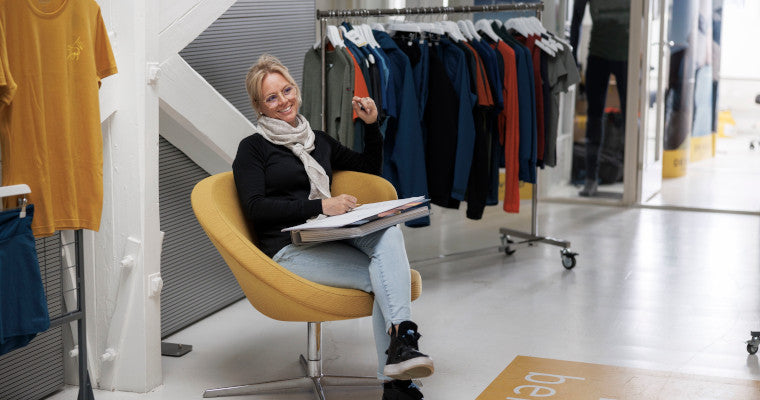 Christine Haraldstad-Sindum sitzt in einem Sessel mit Block und Stift. Neben ihr ist eine Kleiderstange aufgestellt.