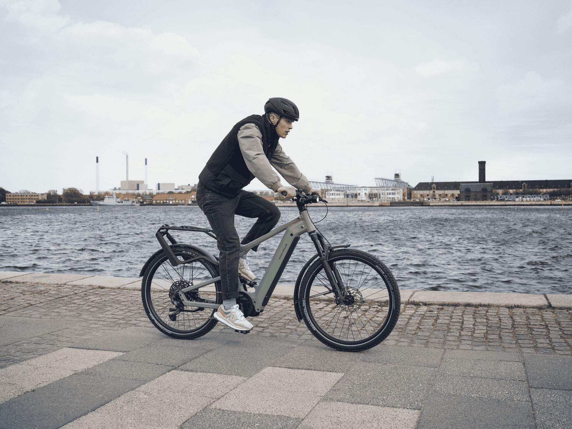 Junger Herr mit Helm auf einem Riese und Müller Fahrrad fährt am Wasser entlang