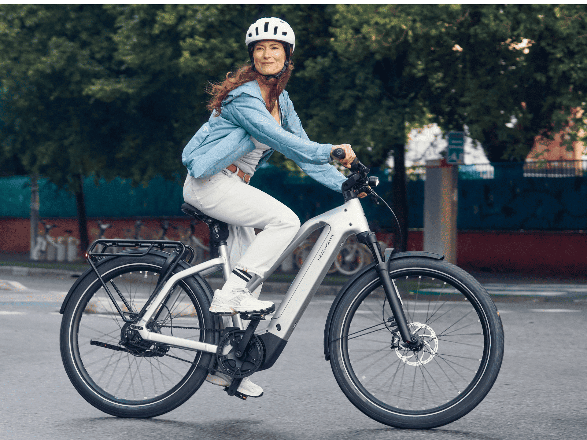 Dame mit Helm fährt auf einem grauen Riese& Müller Fahrrad schaut nach rechts in die Kamera und schmunzelt