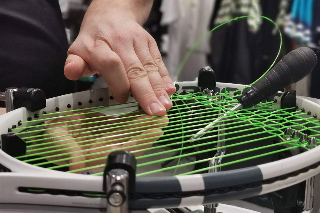 Ein Mitarbeiter bespannt einen Tennisschläger mit grüner Saite.